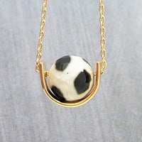 Eclipse Necklace - black white spotted round stone in semicircle pendant, Tibetan Dzi agate bead ball, giraffe print in gold half circle - Constant Baubling